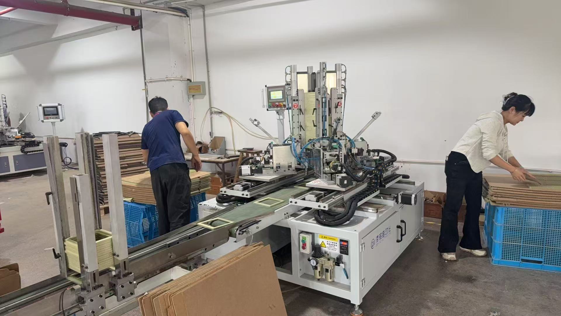Operators working beside frame assembly equipment and stacks of frame components
